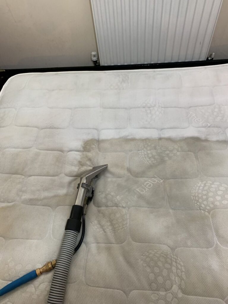 Pneumatic upholstery nailer connected to a gray air hose resting on a white mattress.